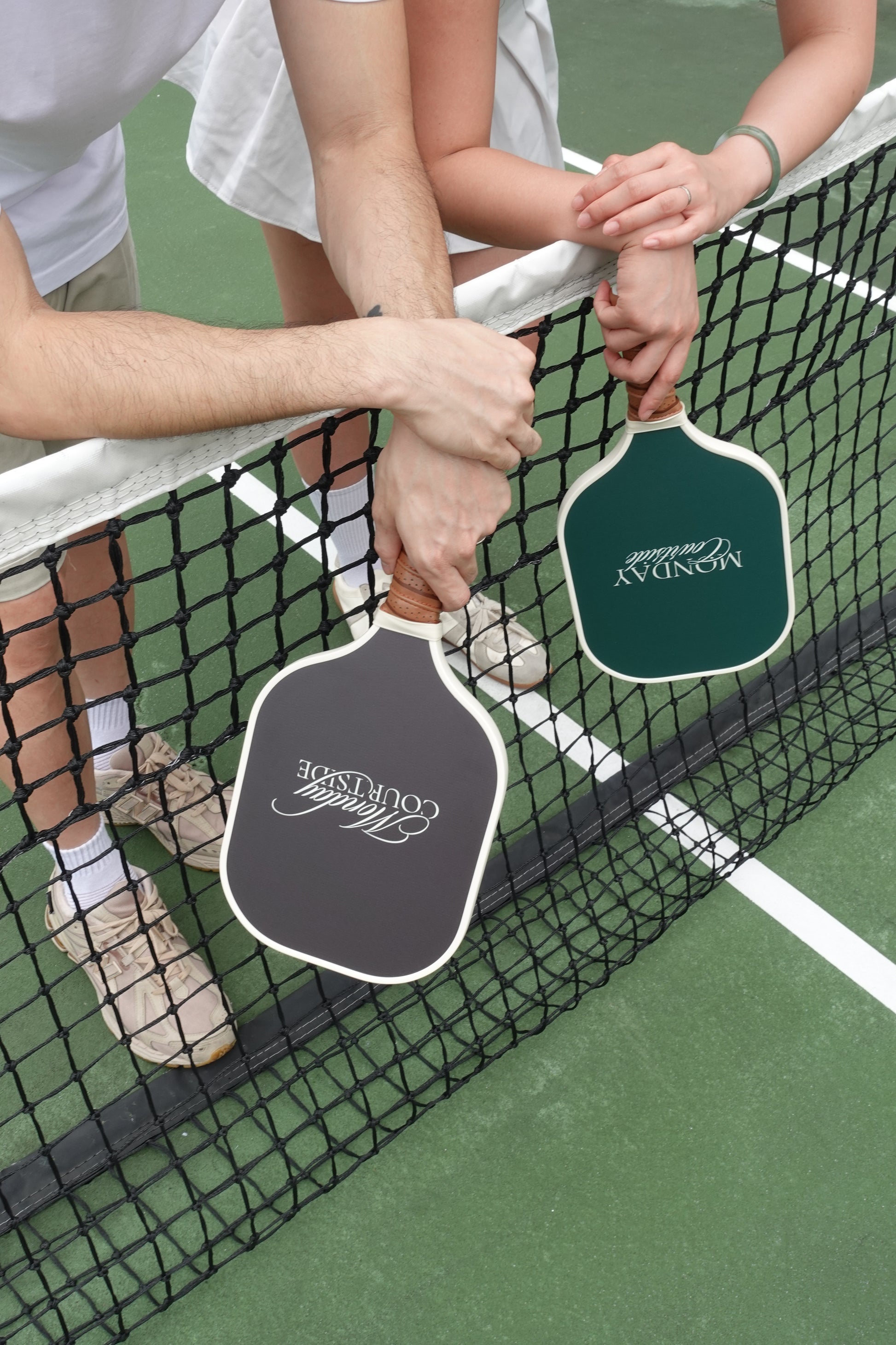 Two hands holding pickleball paddles upside down, highlighting grip and craftsmanship of the Signature Courtside Set