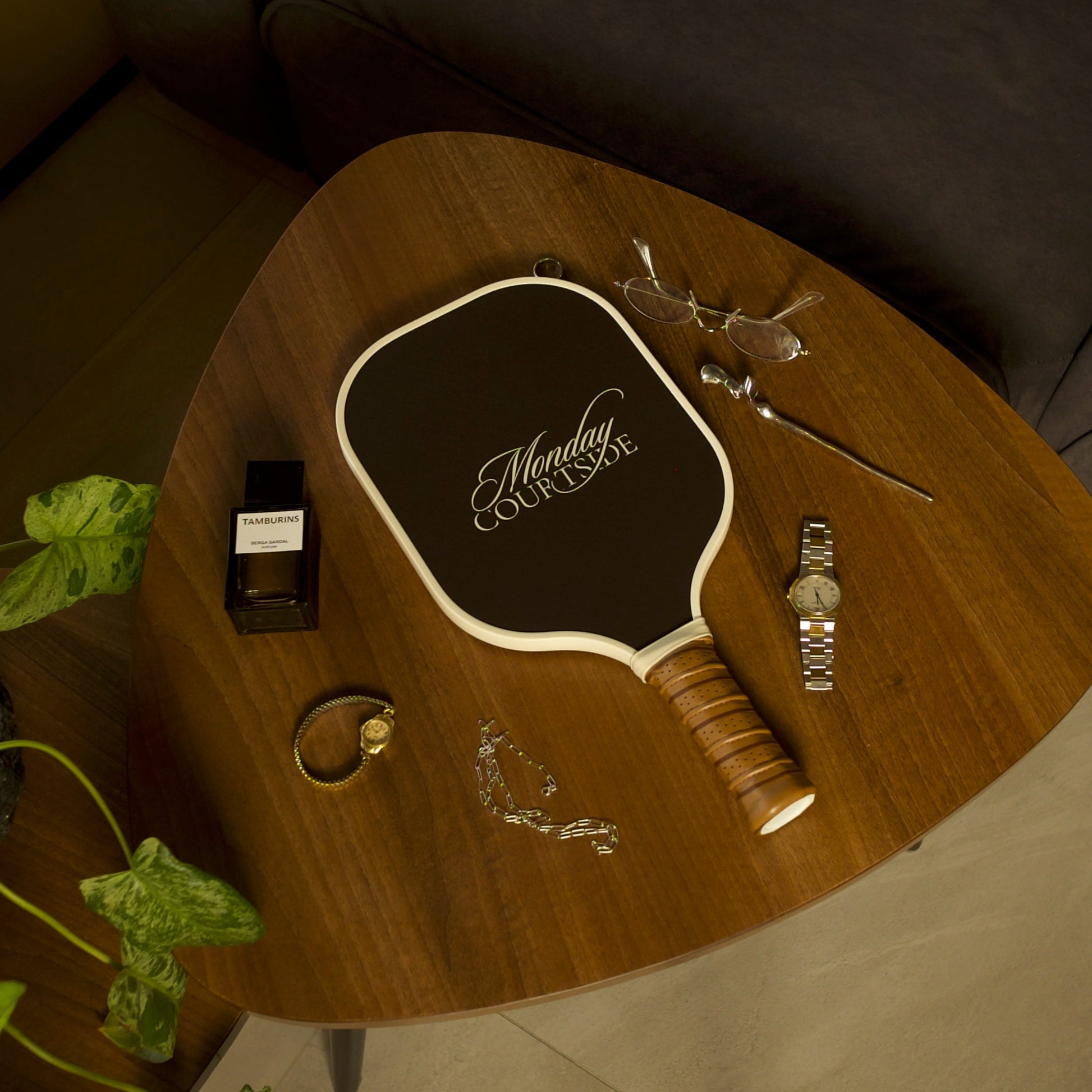 Brown pickleball paddle with branding on a small round table next to a plant and a couch.