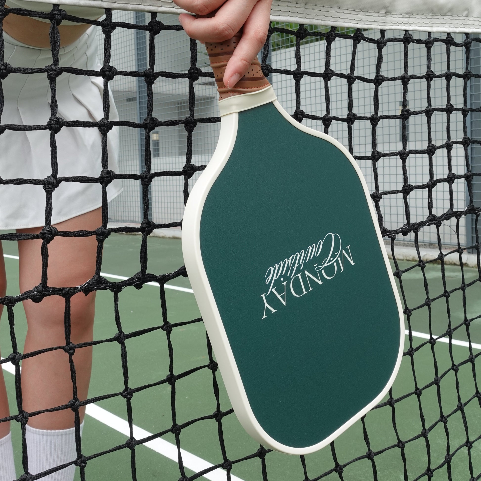 Person holding a green pickleball paddle with branding on a pickleball court.